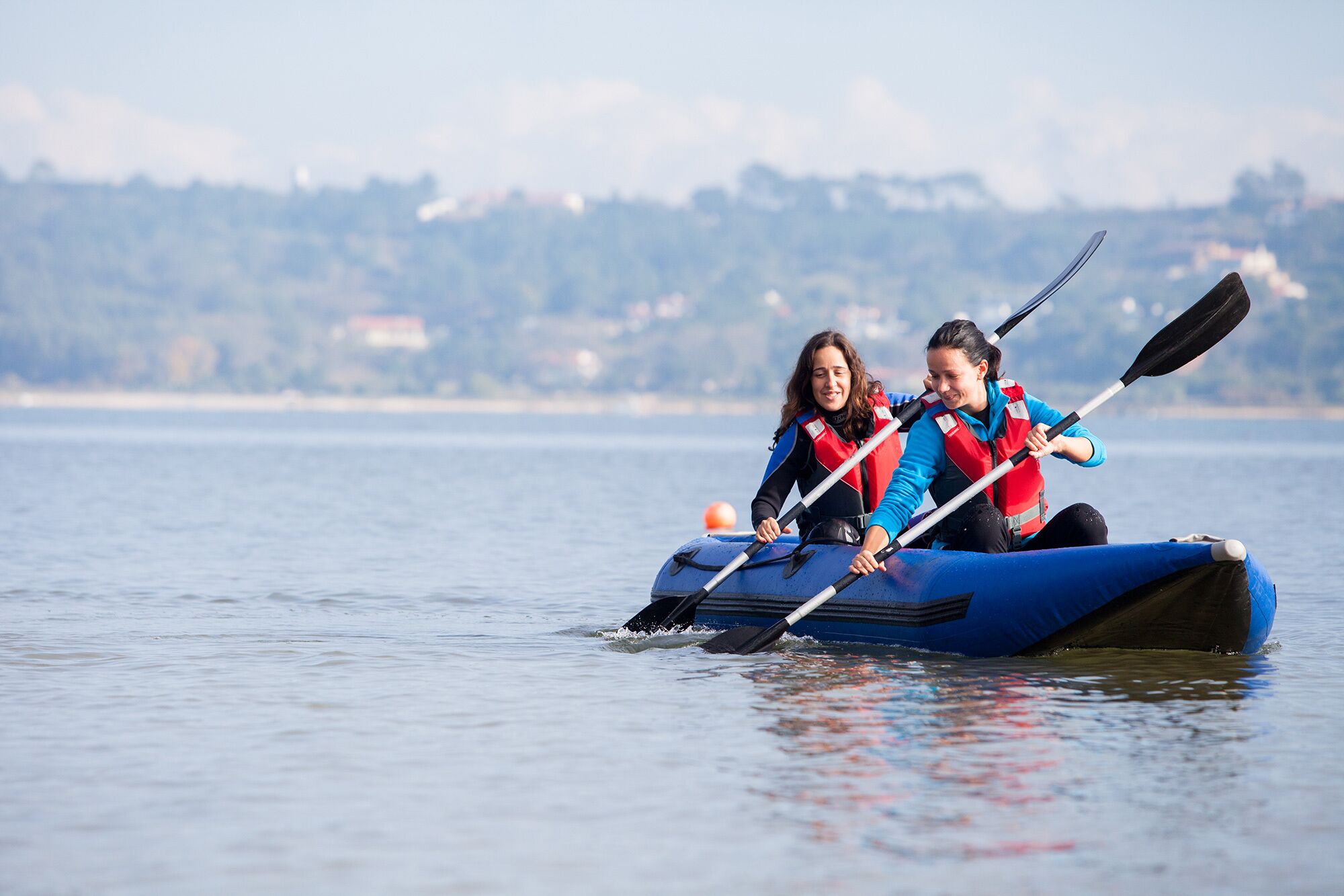 Two people in a blue kayak on calm water with a distant shoreline.