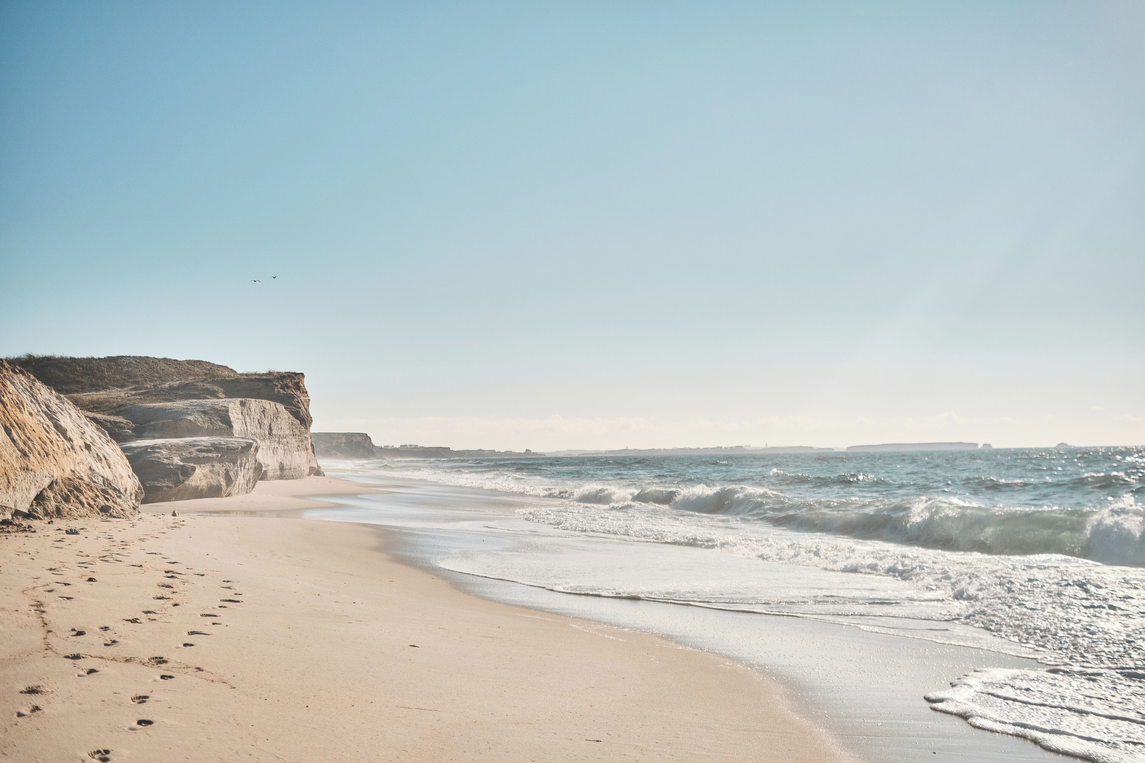 A beach with a sandy shore, waves, and cliffs.