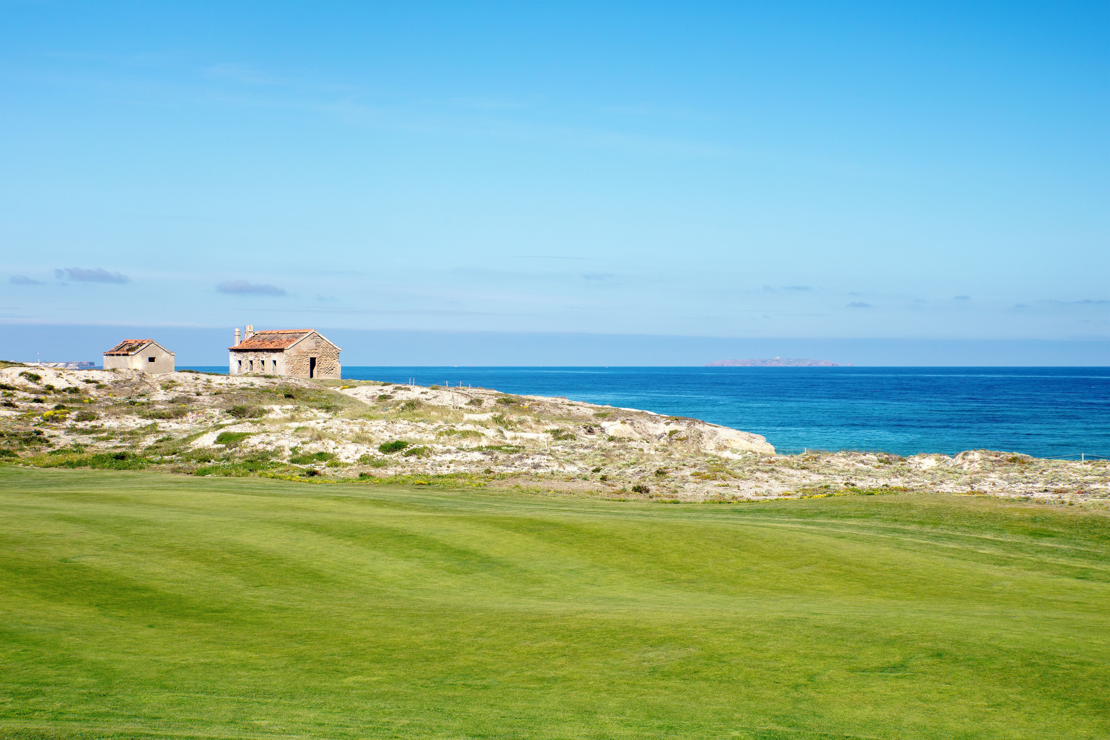 A coastal landscape with a grassy area and two stone buildings.