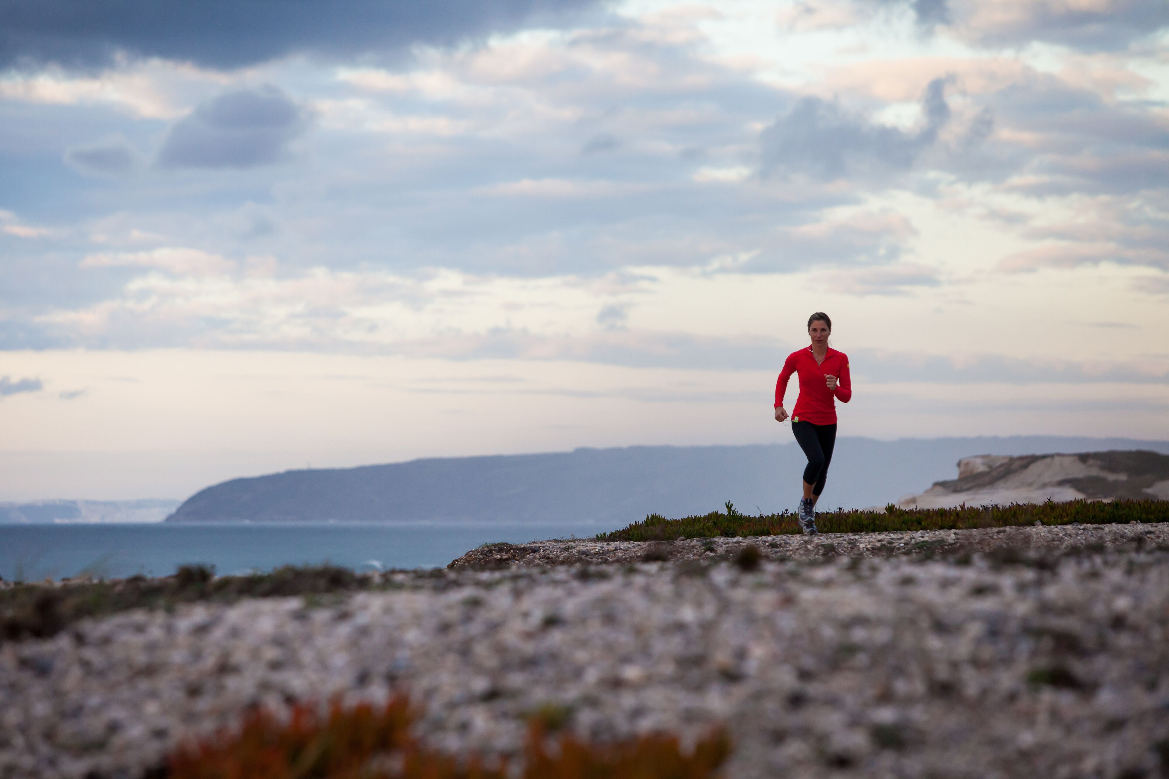 A person running on a rocky terrain with a coastal view in the background.