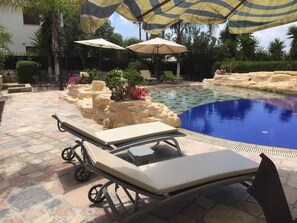 A poolside area with lounge chairs and umbrellas, surrounded by a stone patio and greenery. - De Michanna Properties (Anarita)