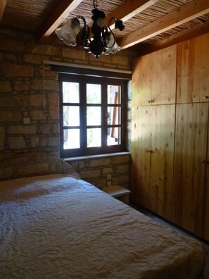 Una habitación con cama, ventana, paredes de piedra, paneles de madera y techo con vigas a la vista.