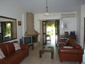 A living room with two brown leather sofas, a television, a fireplace, and a dining table. - De Michanna Properties (Anarita)