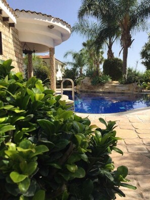 A swimming pool surrounded by lush greenery and a stone building with a tiled roof. - De Michanna Properties (Anarita)