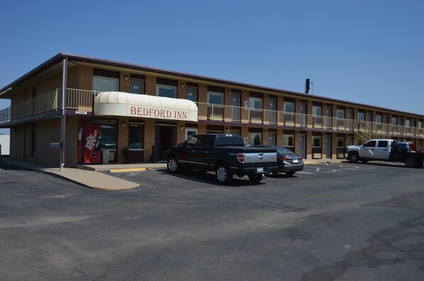 Un motel de dos pisos con un letrero que dice 'BEDFORD INN'. Hay dos coches estacionados al frente y una pequeña rampa que lleva a la entrada.