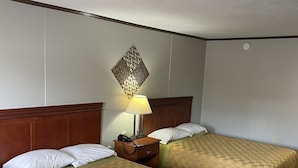 Quarto de hotel com duas camas, uma mesinha de cabeceira com abajur e um objeto decorativo na parede.