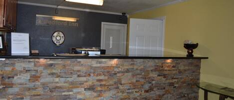 Un área de recepción con pared de piedra, un letrero que dice 'Bedford Inn', una puerta y una pequeña mesa con un cuenco encima.