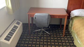 A hotel room with a bed, a desk, a chair, and an air conditioning unit.