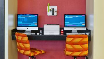 Un espacio de trabajo con dos computadoras Apple iMac, una impresora y dos sillones estampados.