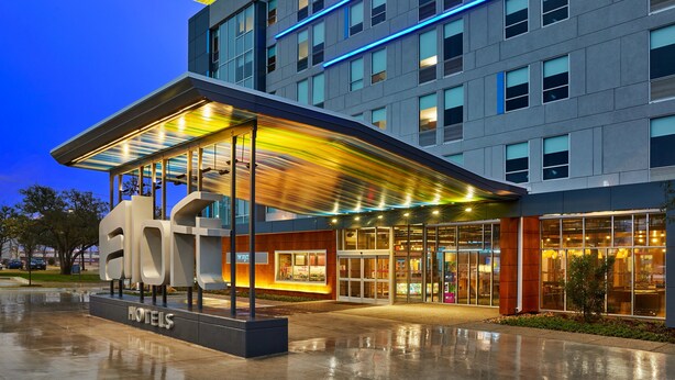 A modern hotel with a glass facade, a covered entrance, and a prominent 'HOTELS' sign. - Aloft by Marriott Austin Northwest (Austin)