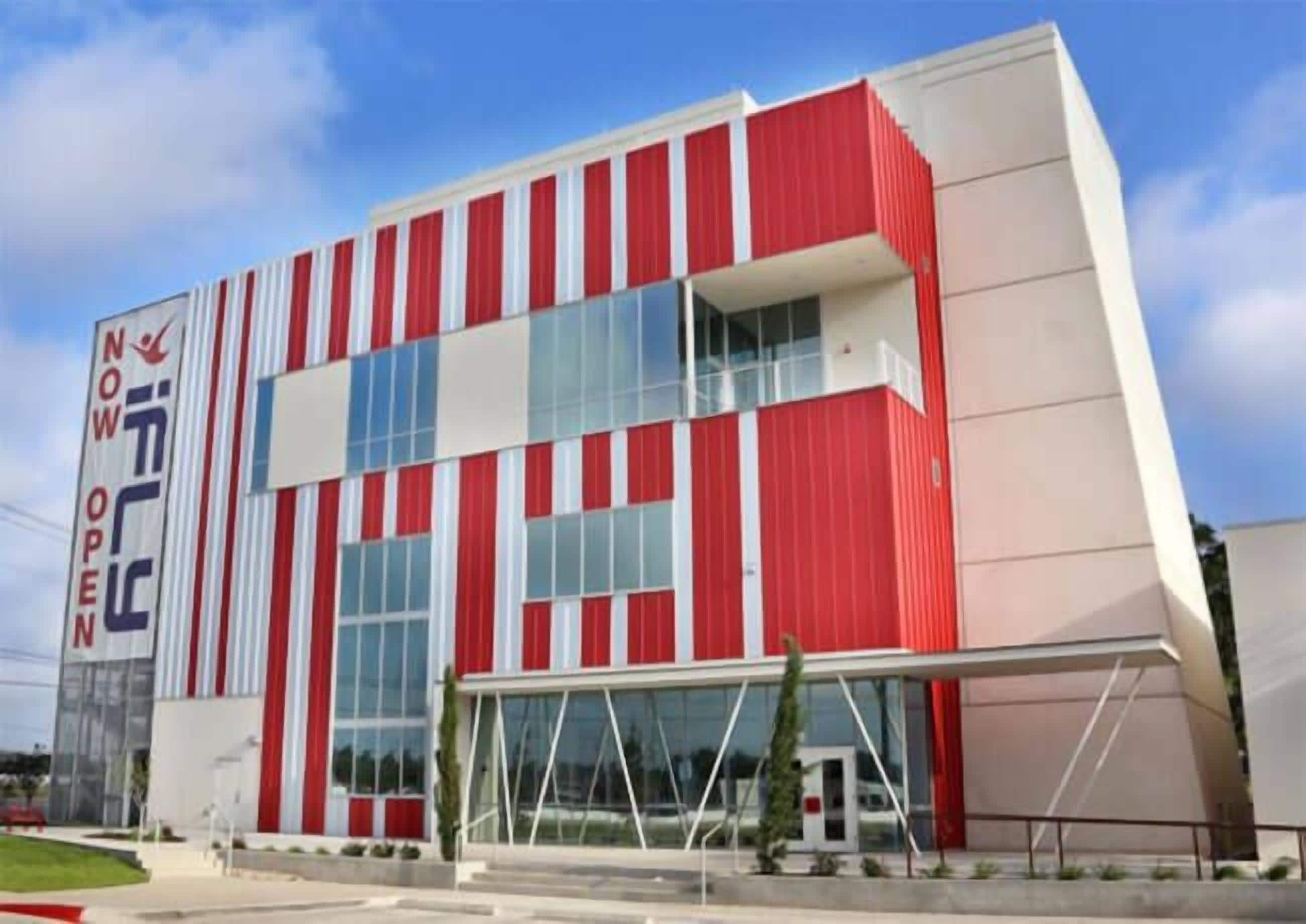 A modern building with a red and white facade, large windows, and a prominent entrance.