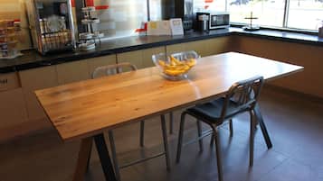 A restaurant with a wooden table, chairs, a fruit bowl, and a coffee machine.