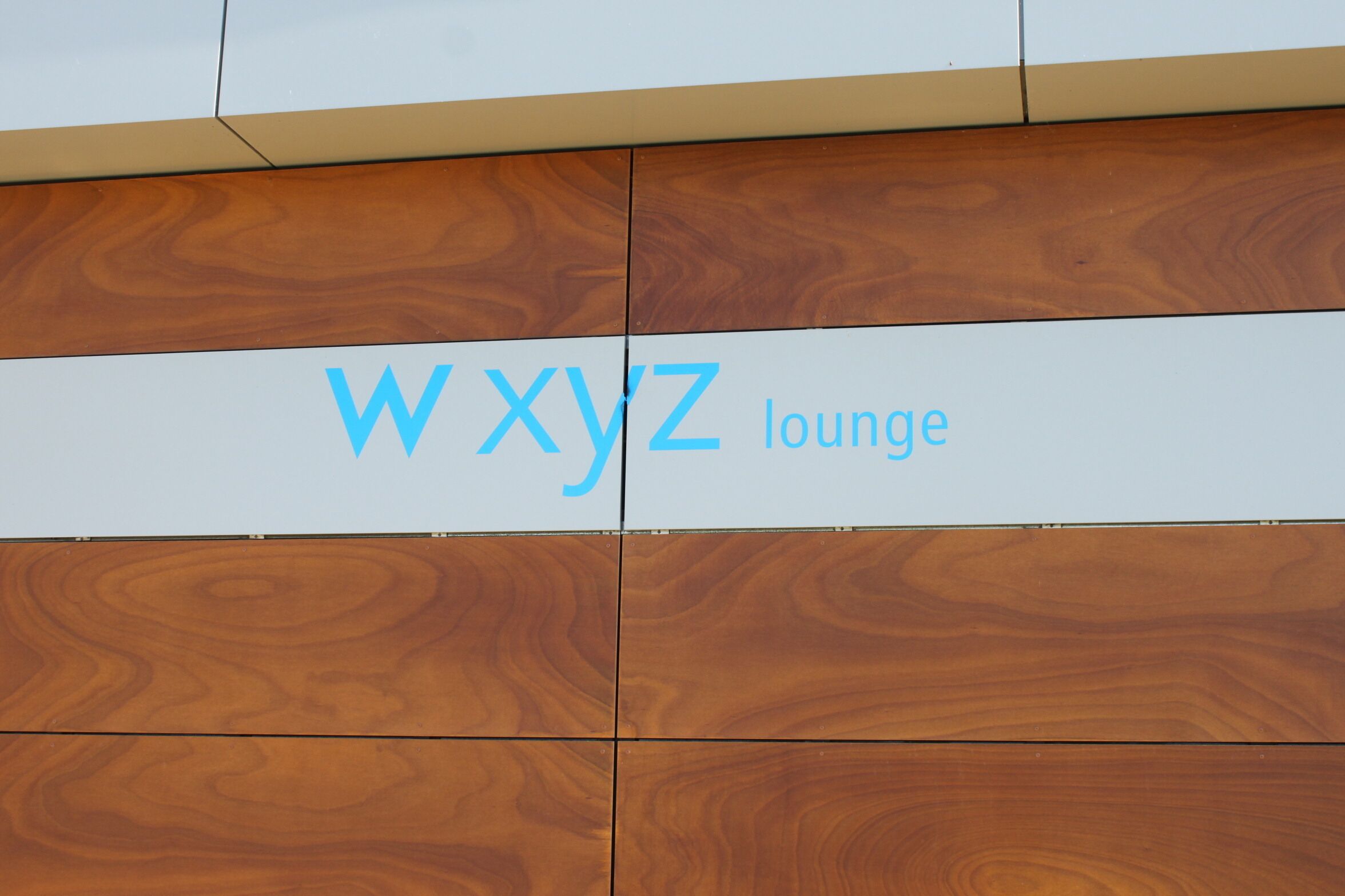 A sign for 'WXYZ Lounge' on a building with a wooden panel design.