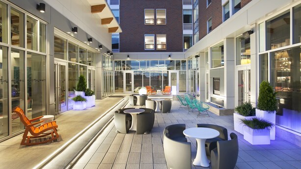 Un espace extérieur moderne, aménagé en terrasse, avec des sièges, des murs en verre et un bâtiment en briques en arrière-plan.