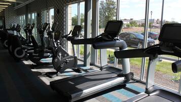 Ein Fitnessraum mit mehreren Laufbändern und Ergometer, großen Fenstern und Blick ins Freie.