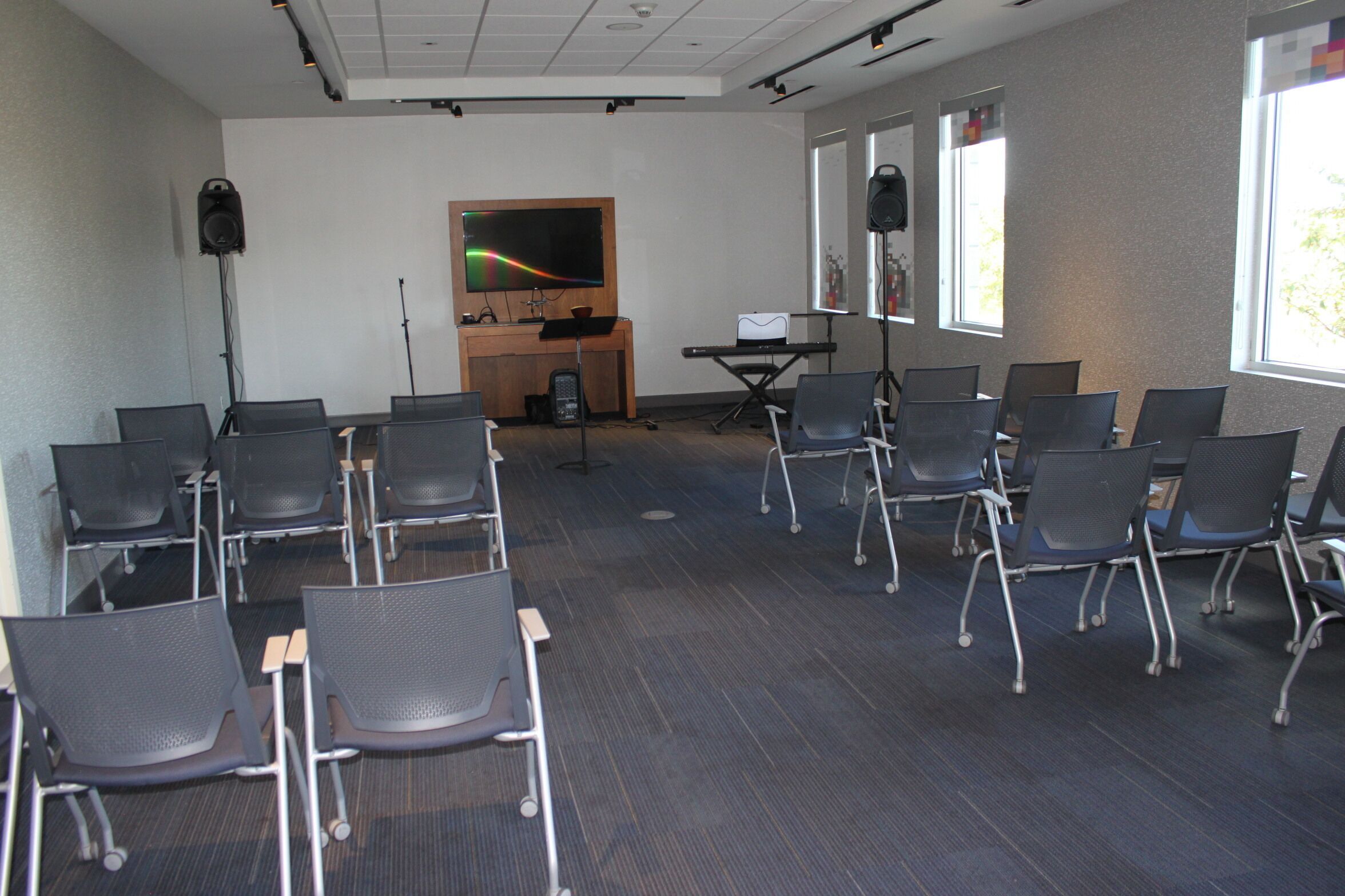 A conference room with rows of chairs, a podium, a large screen, and a speaker.