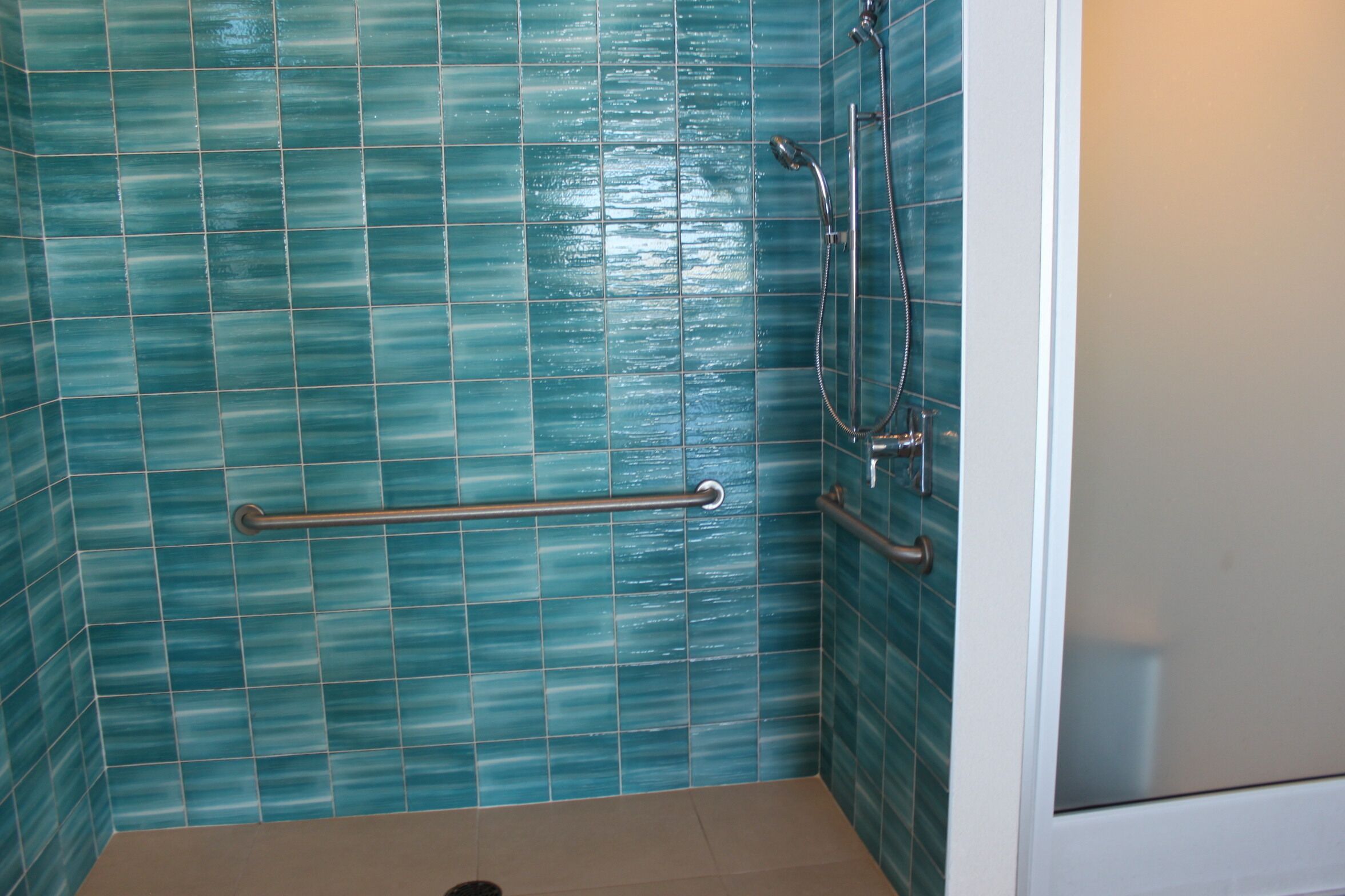 A bathroom with a blue-tiled wall, a grab bar, and a shower fixture.
