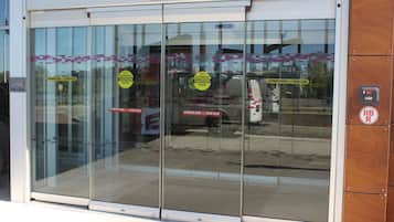 A glass door with multiple stickers indicating "Automatic Door - Stand Clear" and a "No Parking" sign.