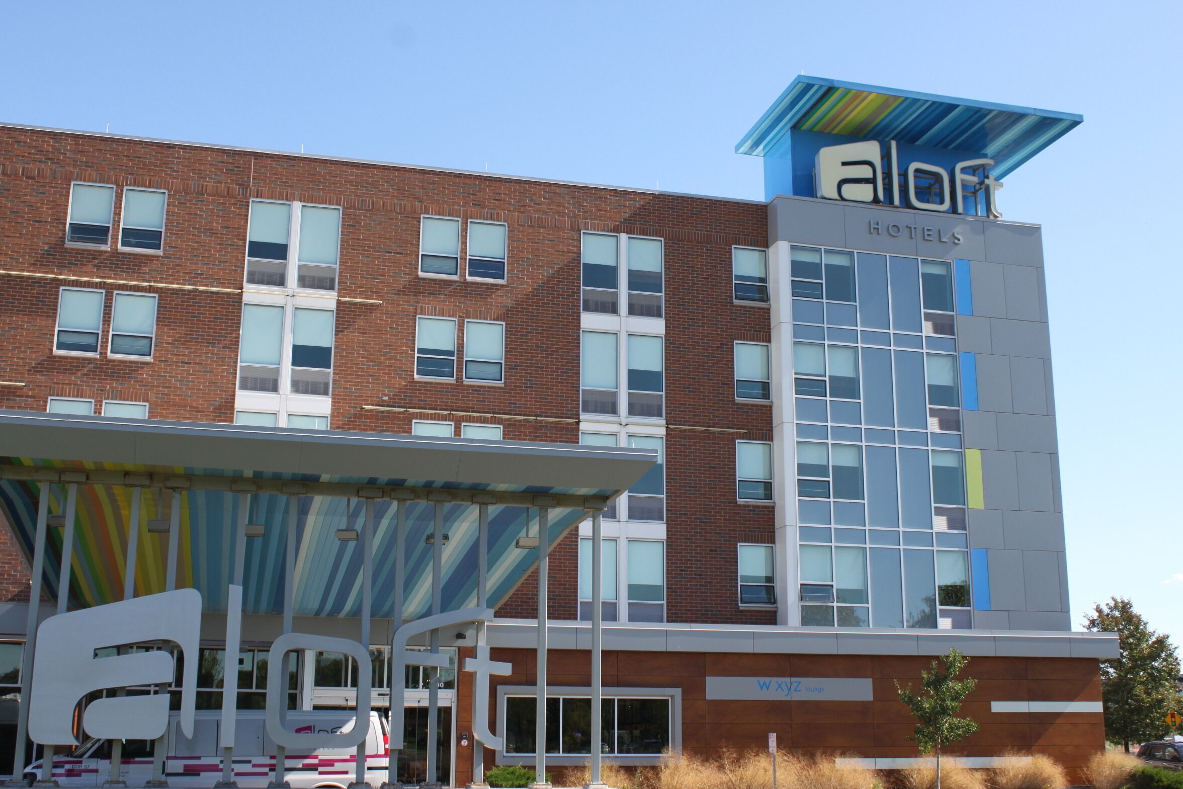 A modern hotel building with a prominent 'aloft' sign, multiple windows, and a covered entrance area.