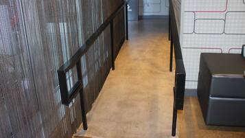 A narrow hallway with a textured wall on one side and a patterned wall on the other. There is a black bench on the right and a door at the end of the hallway.