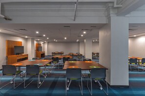 A conference room with multiple tables and chairs, a wooden panel wall, and a television. - Aloft by Marriott Houston Downtown (Houston)