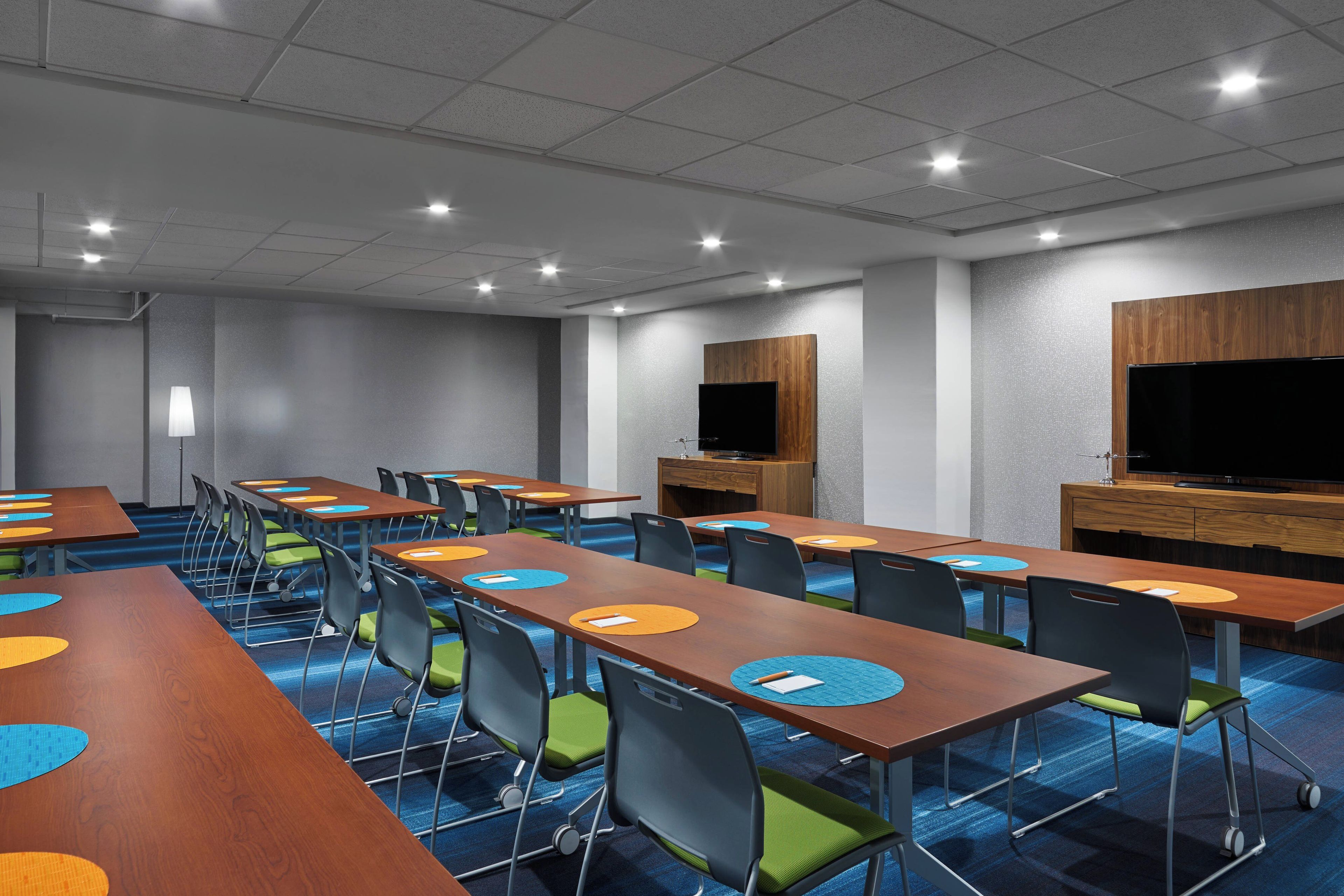 A conference room with multiple tables and chairs, equipped with built-in screens and a flat-screen TV on the wall.