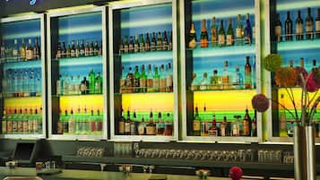 A bar area with multiple shelves of liquor bottles, a neon sign, and a bar counter with chairs and a cash register.
