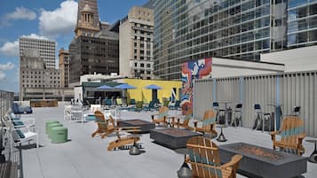 An outdoor seating area with various chairs and tables, a fire pit, and a view of surrounding buildings.
