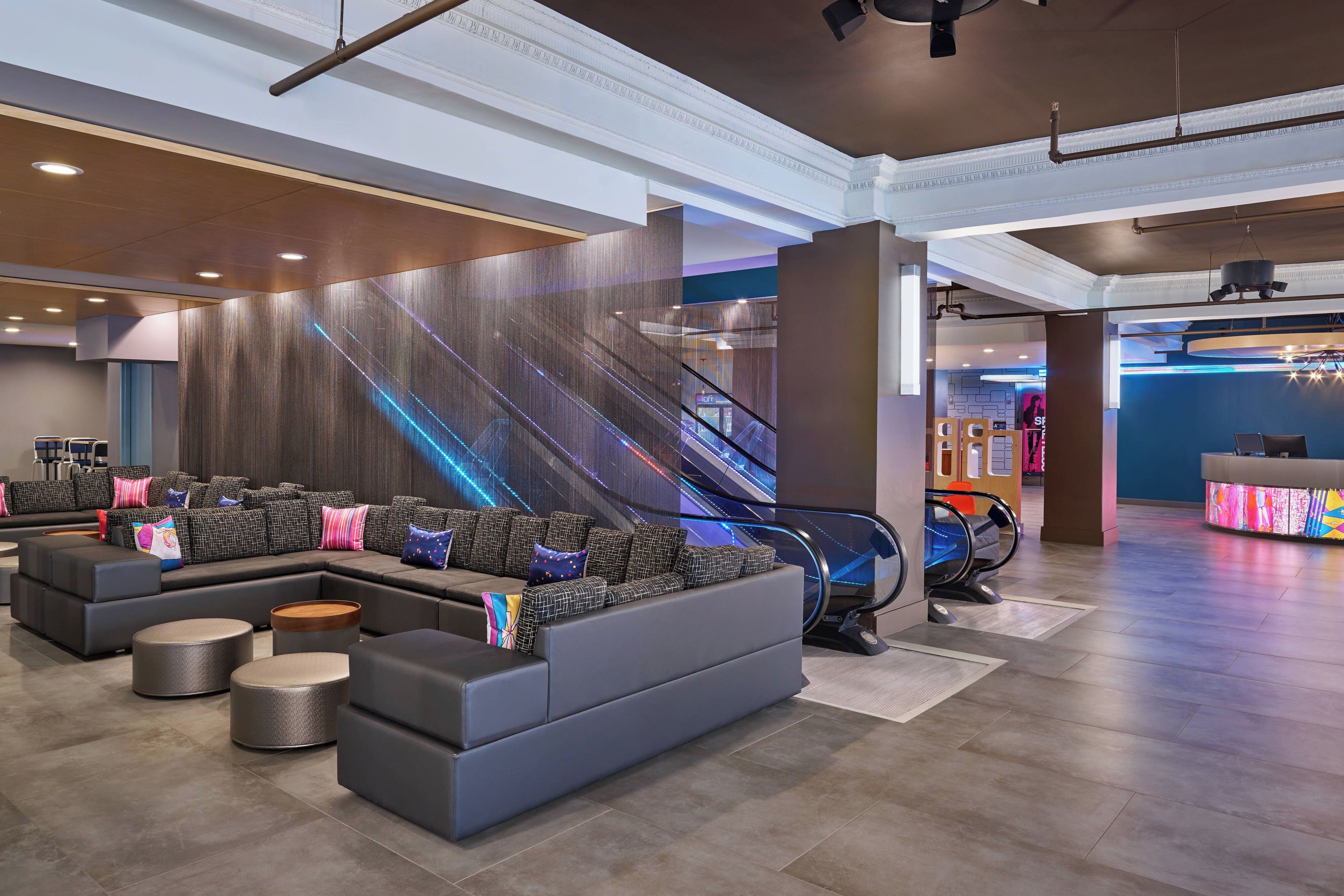 A modern lobby with a seating area, escalators, and a reception desk.