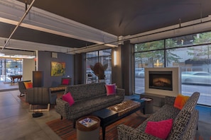 A modern lounge area with sofas, a fireplace, and large windows offering a view of the street. - Aloft by Marriott Houston Downtown (Houston)