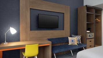 Een moderne hotelkamer met een houten bureau, een blauwe bank, een aan de muur bevestigde televisie en een kledingkast met hangruimte.