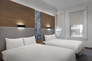 Habitación de hotel con dos camas, cabecera de madera, pared con diseño y ventana con persianas.