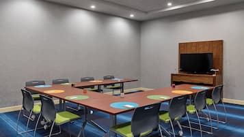 A conference room with a large table, chairs, a television, and a wooden cabinet.