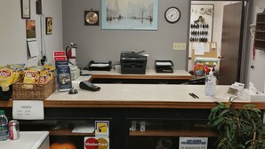A reception desk with a framed cityscape picture, a clock, and a bulletin board with hanging items. - Jubilee Motor Inn (Davidson)
