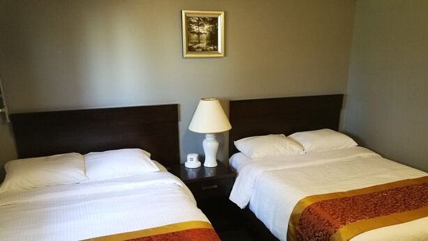 A hotel room with two beds, each with white linens and a red and gold bedspread. There is a nightstand with a lamp between the beds. A framed picture hangs on the wall above the beds. - Jubilee Motor Inn (Davidson)