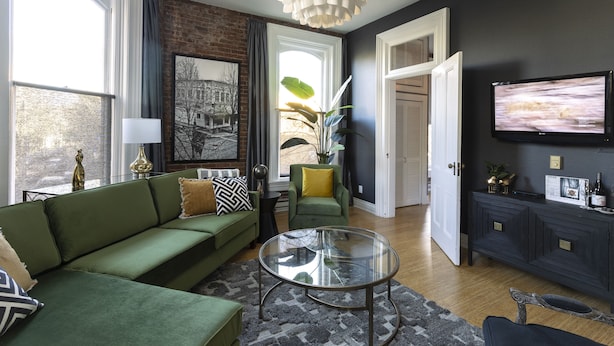 A living room with a green sofa, a glass coffee table, and a TV mounted on the wall.