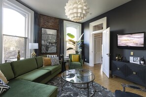 A living room with a green sofa, a glass coffee table, and a TV mounted on the wall.
