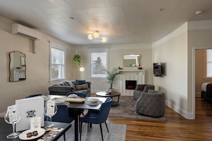 A living room with a fireplace, seating area, and a dining table with wine glasses. - 3rd Street Flats (McMinnville)