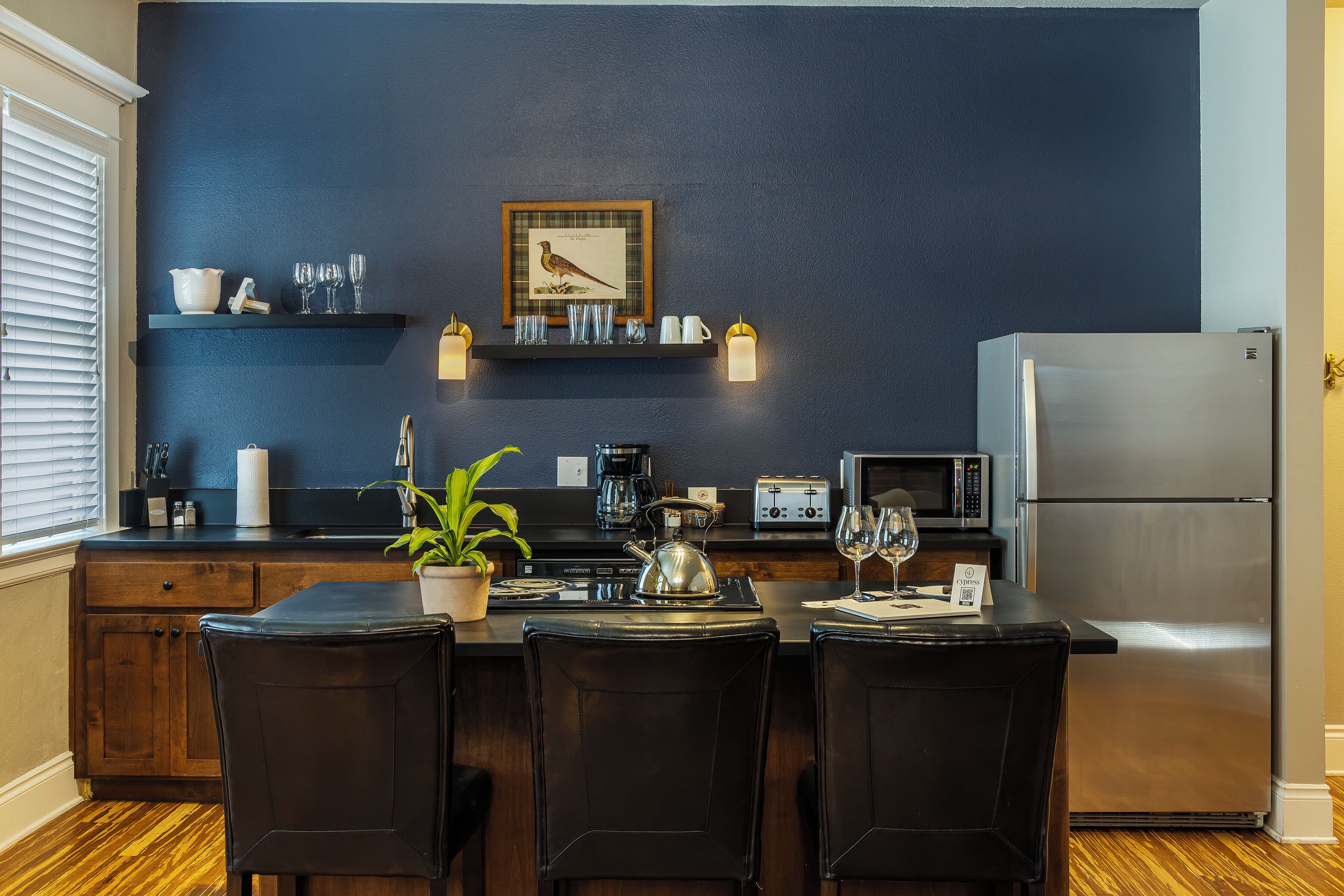 Una cucina moderna con una parete blu scuro, mobili in legno, un frigorifero in acciaio inossidabile e un'area pranzo con sedie nere.