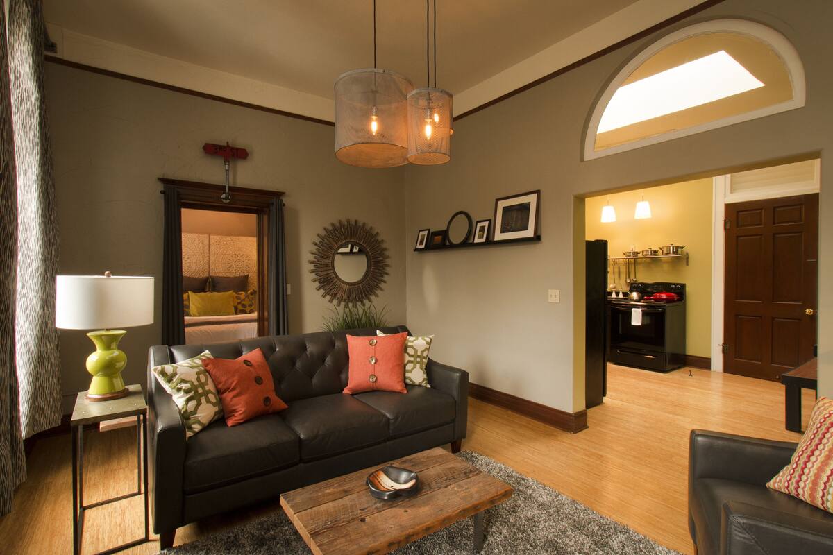 A living room with a black leather sofa, a wooden coffee table, and a dining area with a kitchen in the background.