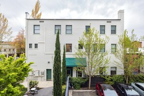 A white building with multiple windows, a green awning, and a parking area with cars. - 3rd Street Flats (McMinnville)