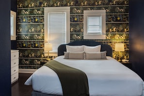 A bedroom with a large bed, two bedside tables, a dresser, and a window with blinds. - 3rd Street Flats (McMinnville)