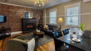A living room with a fireplace, a television, a sofa, and a dining table with wine glasses and a plant.