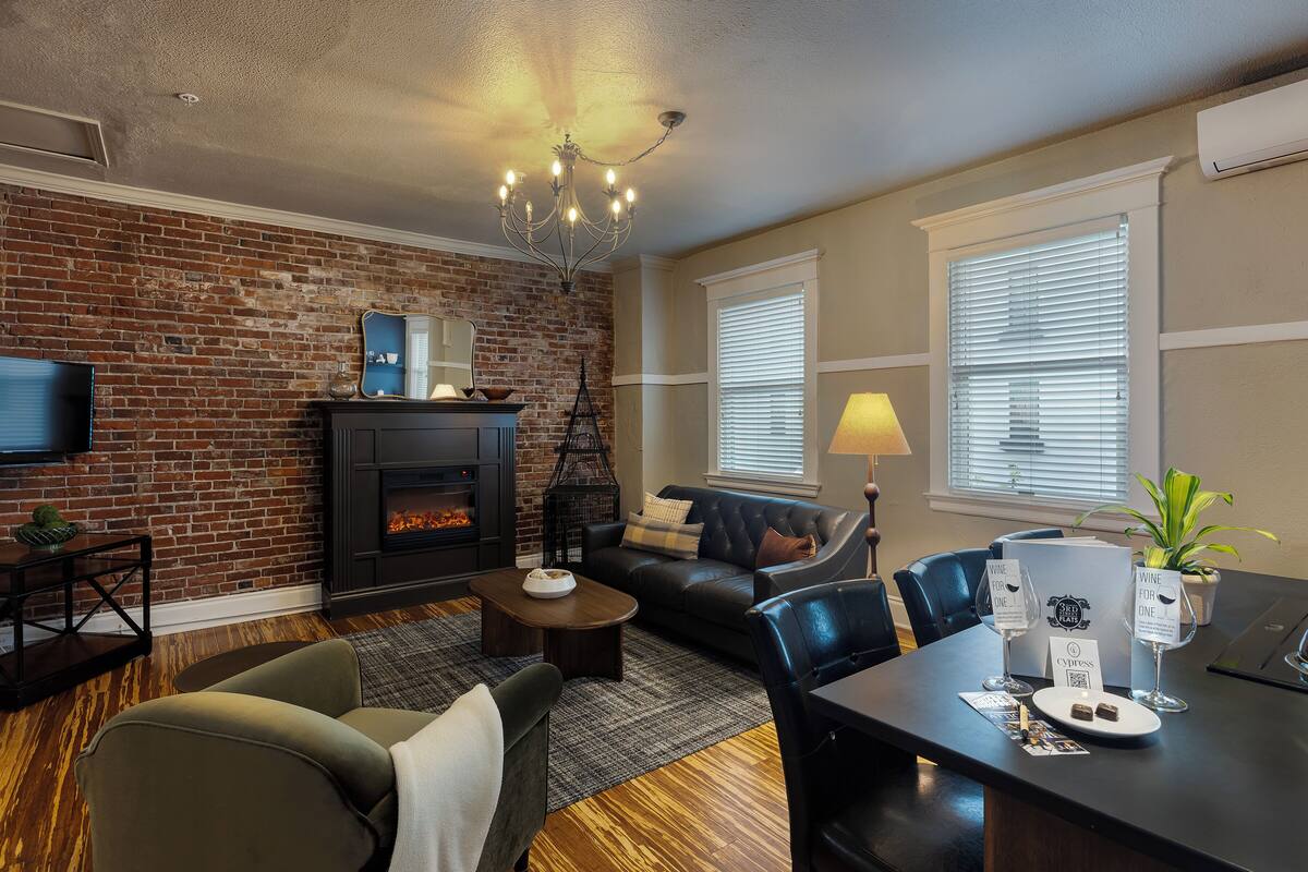 A living room with a fireplace, a television, a sofa, and a dining table with wine glasses and a plant.