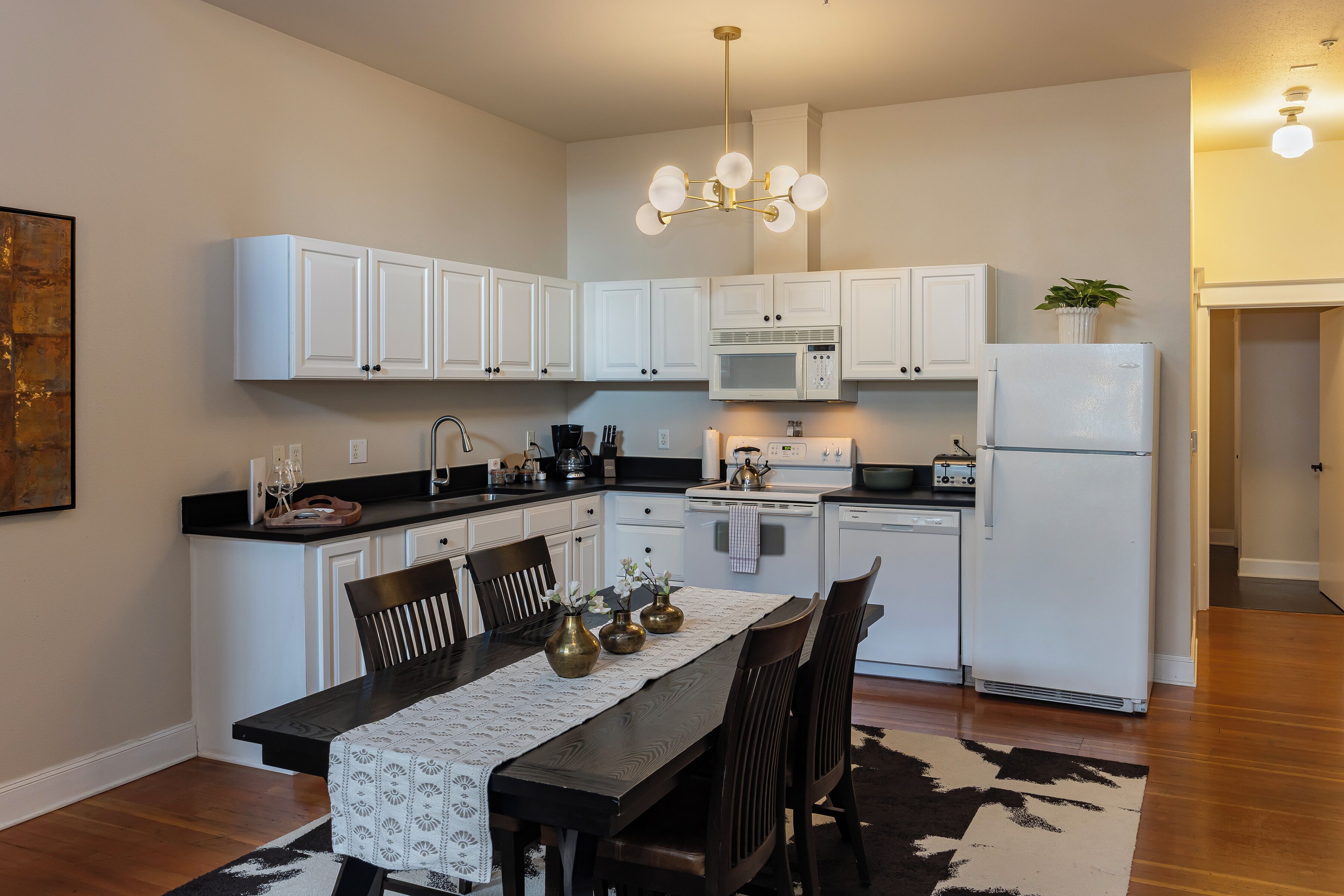 Una cocina moderna con armarios blancos, una isla central con asientos, una mesa de comedor con mantel de encaje y una alfombra blanco y negro.