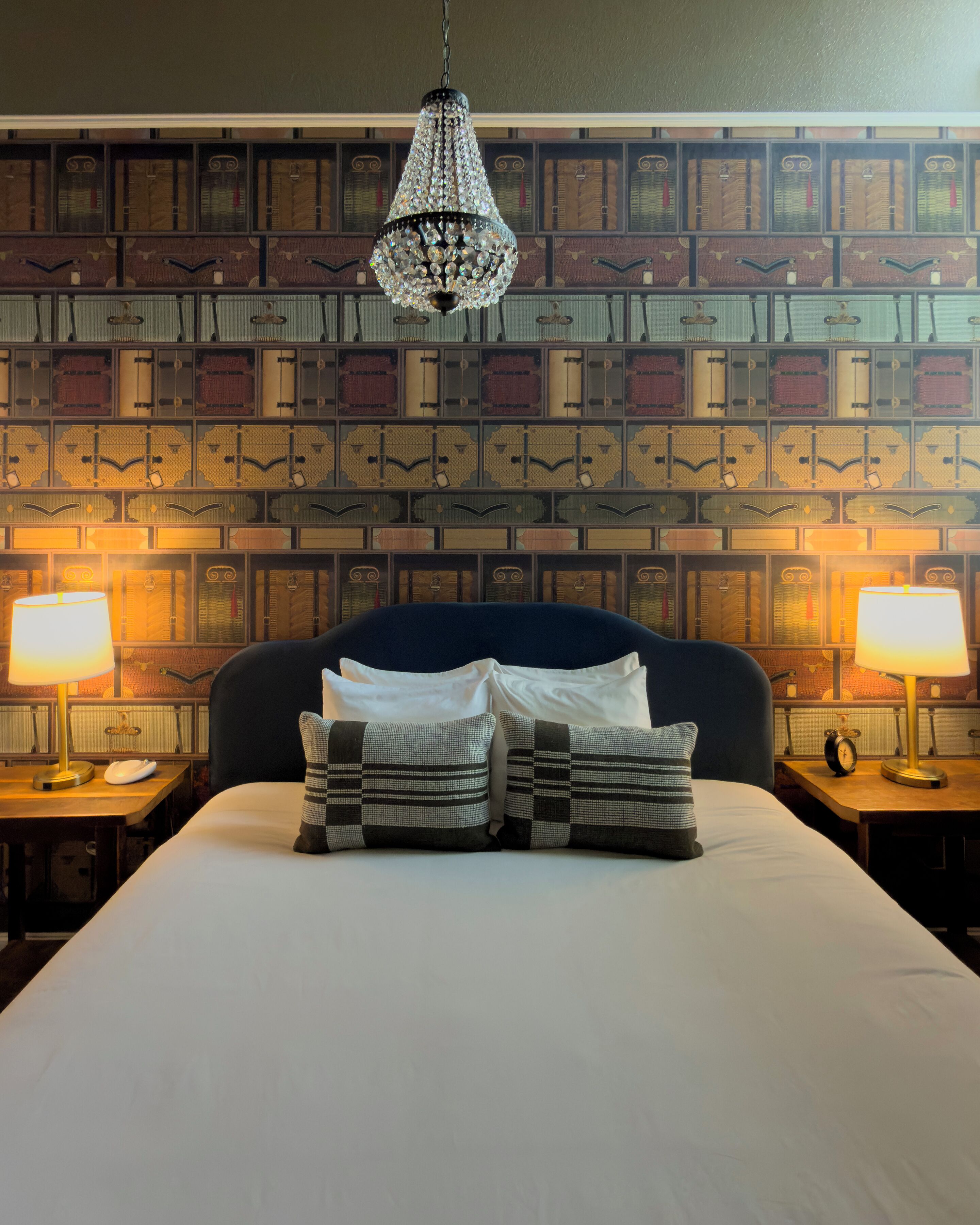 A neatly made bed with pillows, a hanging chandelier, and a wall with patterned wallpaper.