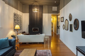 A modern living room with a fireplace, a sofa, a coffee table, and a chandelier. - 3rd Street Flats (McMinnville)