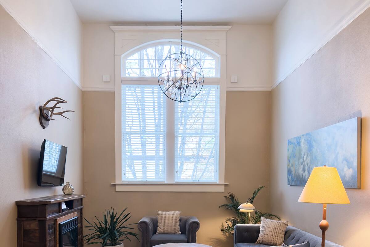A living room with a fireplace, two sofas, a coffee table, a chandelier, and a large window.