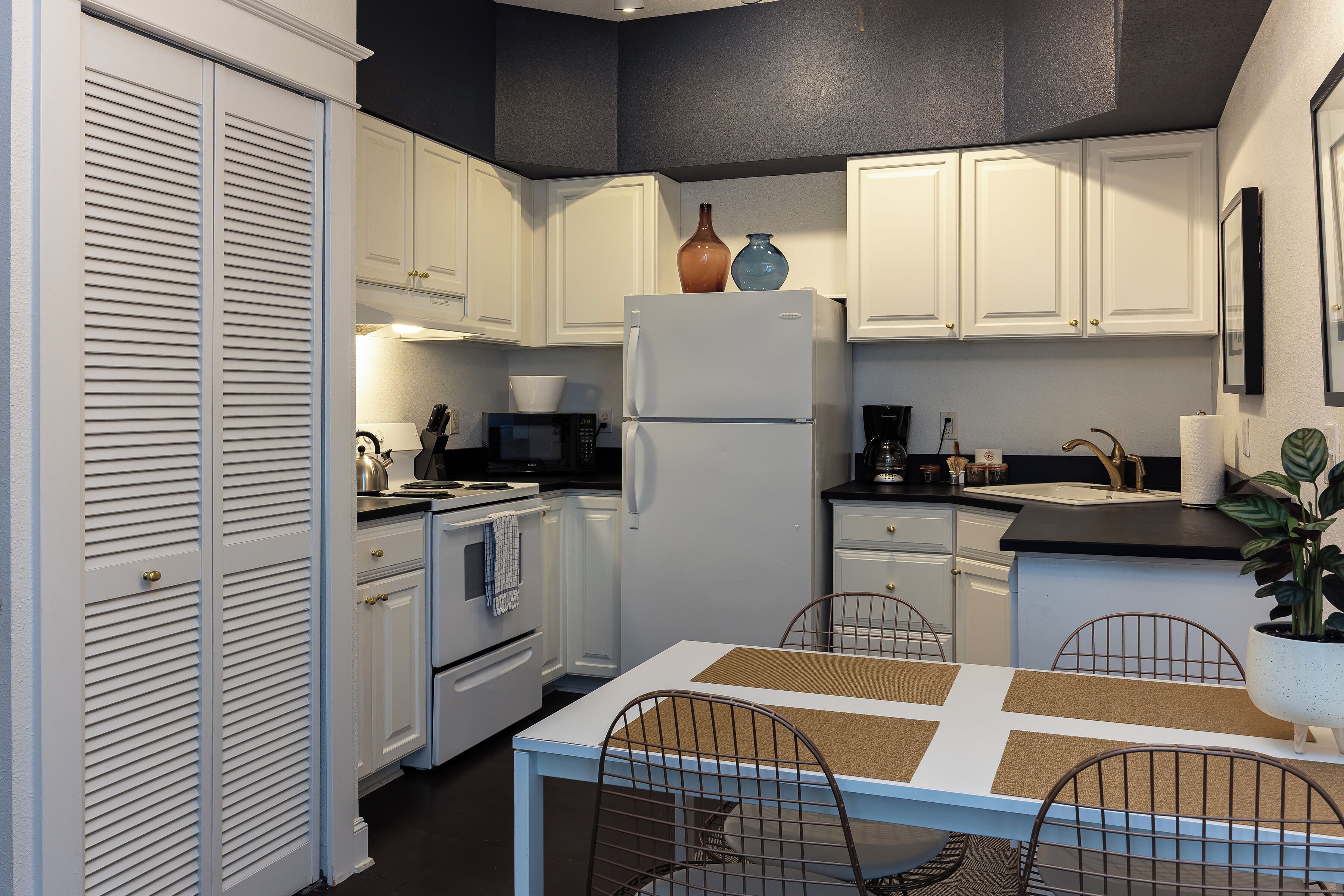A kitchen with white cabinets, a white refrigerator, a microwave, and a dining table with chairs.