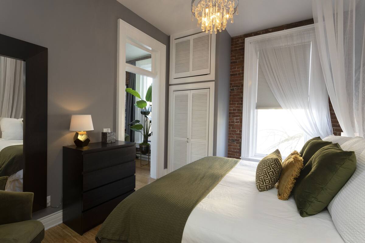 A bedroom with a bed, a dresser, a lamp, a mirror, and a window with curtains.